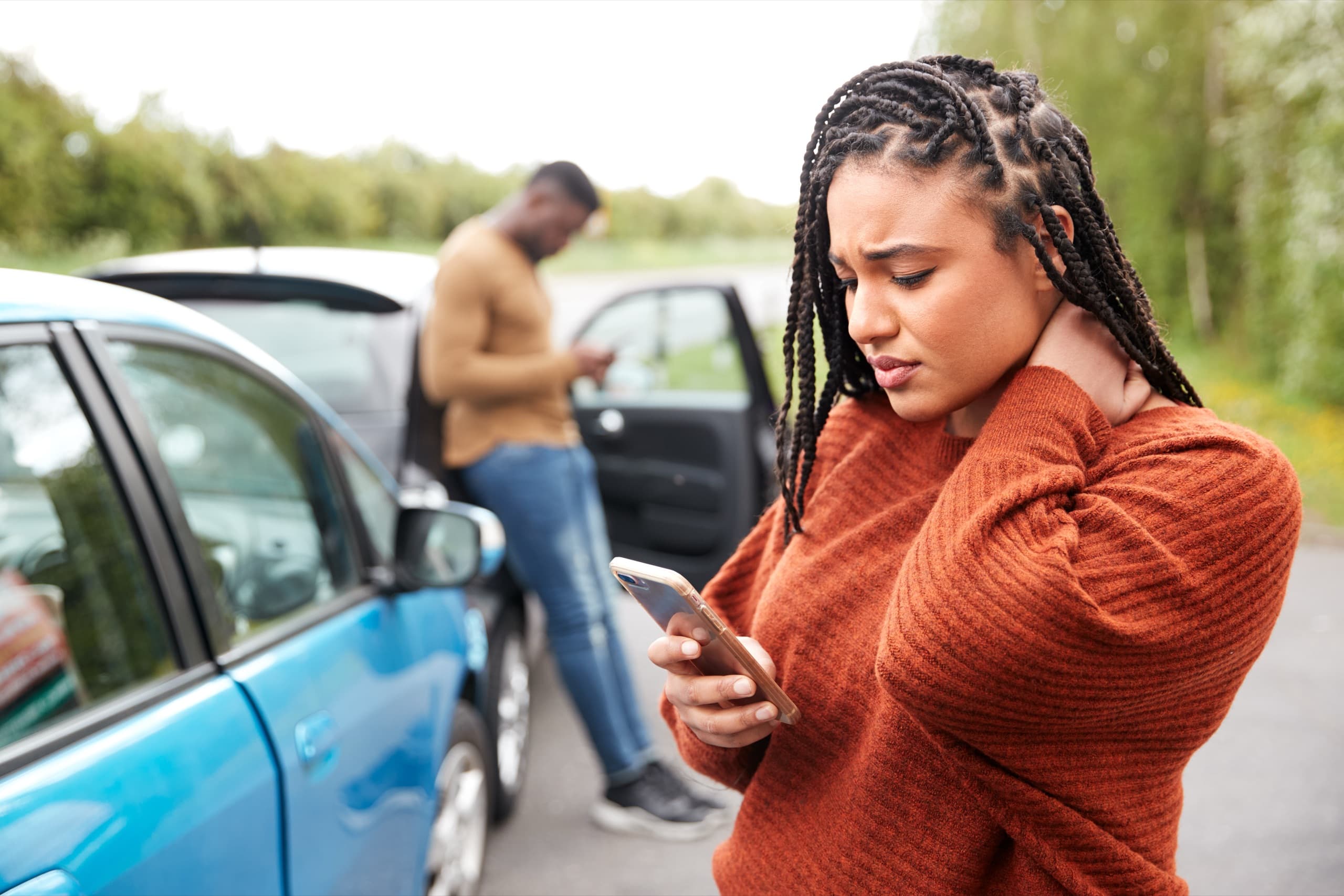 Woman holding her neck beside her car after an auto accident